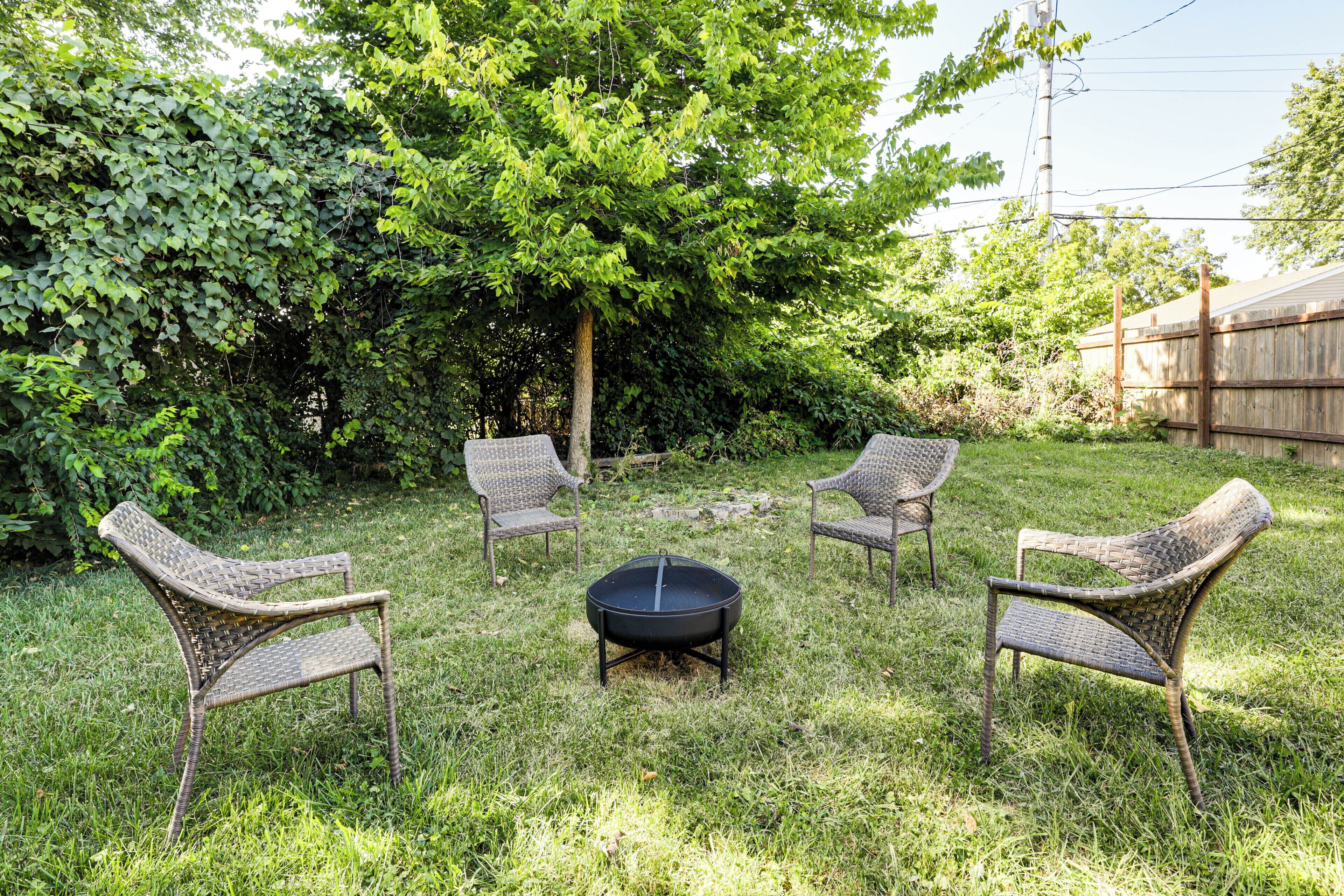 A backyard with a fire pit, three wicker chairs, and a wooden fence.
