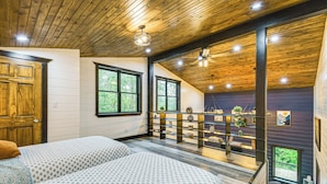 Quarto com duas camas, teto de madeira, janelas amplas e varanda com plantas.