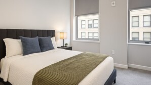 A neatly made bed with a dark headboard, two pillows, a green throw blanket, and a nightstand with a lamp.