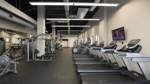 A gym with treadmills, weight machines, and a TV on the wall.