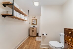 A bathroom with wooden shelves holding towels, a sink with a mirror, a toilet, and a wooden cabinet.