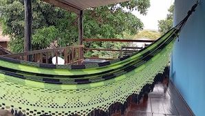 A hammock under a wooden ceiling with a view of trees and a building in the background. - New Dawn. (Alto Paraíso de Goiás)