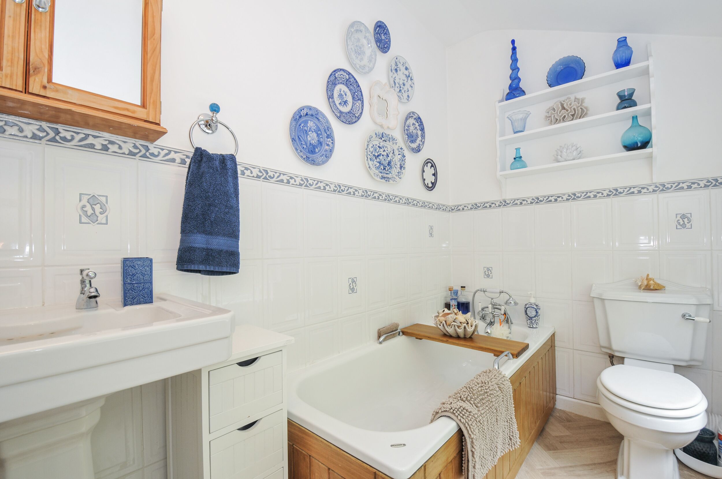 A bathroom with a white sink, a bathtub, a toilet, and decorative plates on the wall.