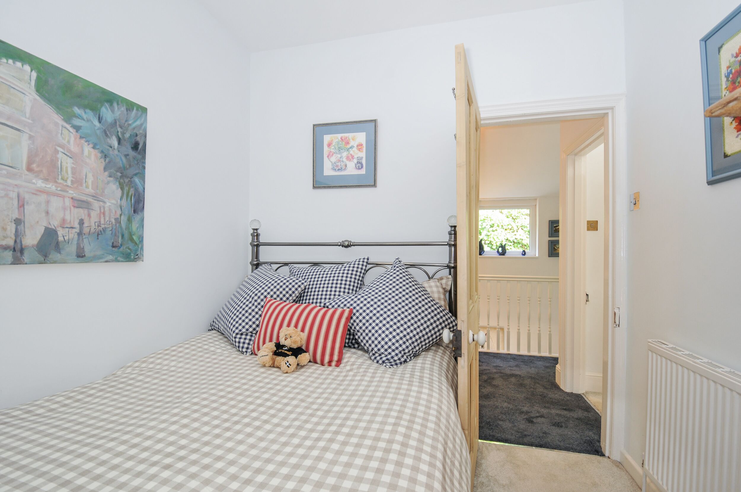 A bedroom with a checkered bedspread, a teddy bear, and a painting on the wall.