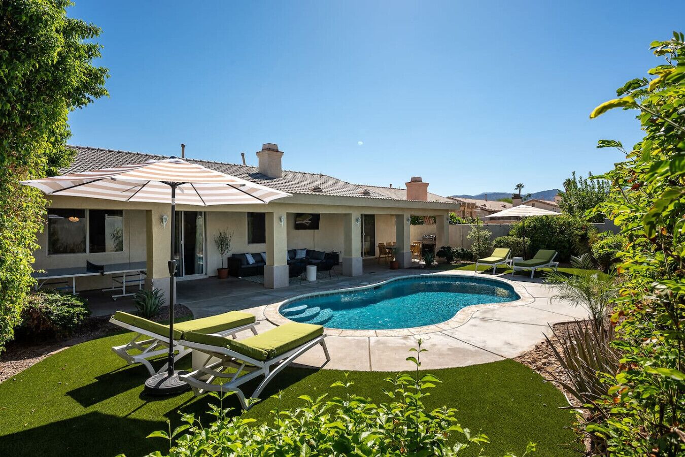 A residential backyard with a swimming pool, patio furniture, and a covered seating area.