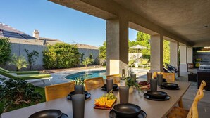 An outdoor dining area with a view of a swimming pool and greenery. - Luma House | Stylish Getaway w/ Game Room & Pool[Free Early Check-In OR Late Checkout] (Indio)