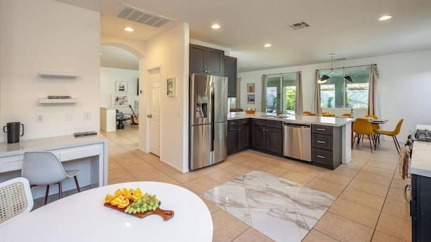 A modern kitchen with a central island, stainless steel appliances, and a dining area with yellow chairs. - Luma House | Stylish Getaway w/ Game Room & Pool[Free Early Check-In OR Late Checkout] (Indio)