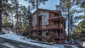 Un edificio de varios pisos de piedra con un balcón de madera, rodeado de altos pinos y nieve en el suelo.