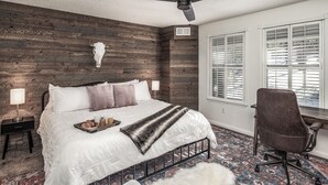 Un dormitorio con cama, escritorio, silla, ventilador de techo y ventana con persianas.
