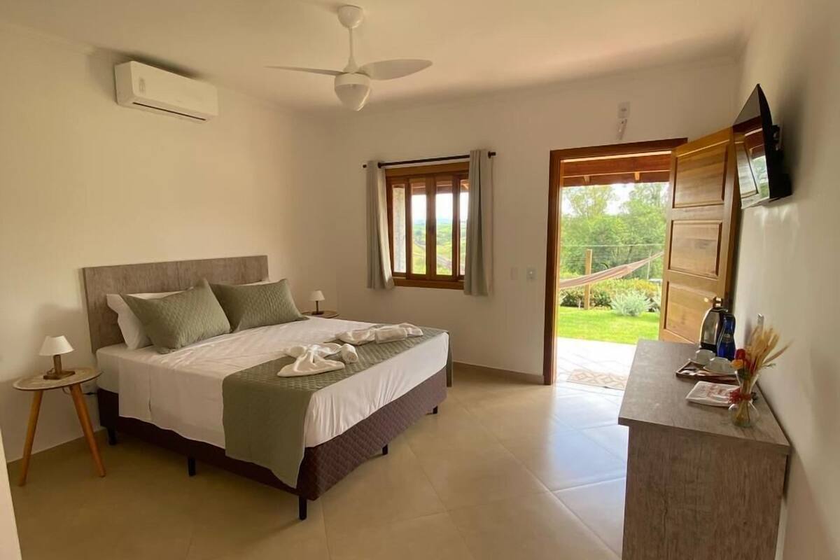 A bedroom with a bed, a nightstand, a desk, a ceiling fan, and a window with curtains.