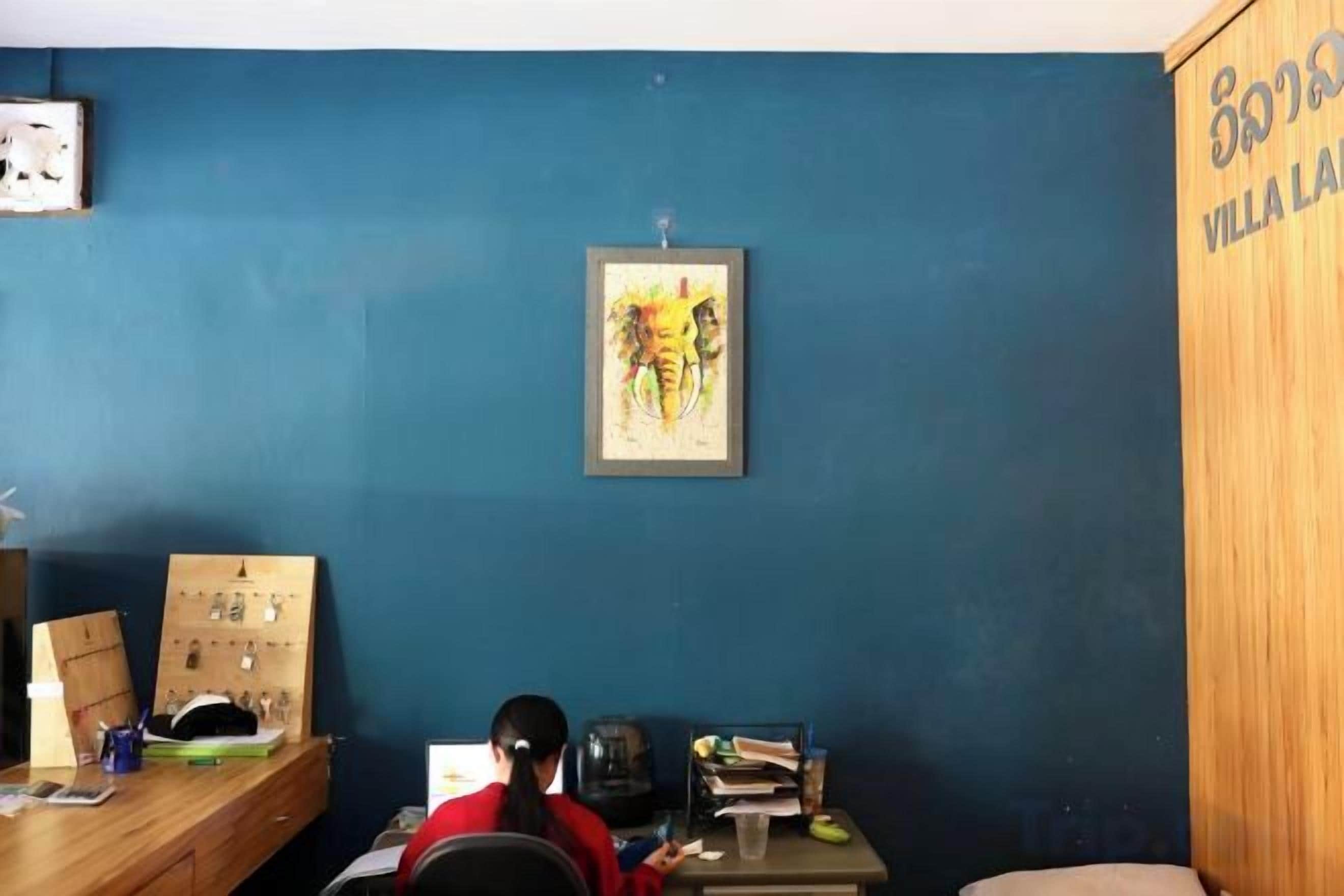 A room with a blue wall, a wooden cabinet, a desk with a computer, and a framed picture on the wall.