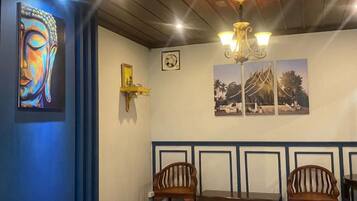 A room with a wooden ceiling, a chandelier, a Buddha painting, and a bench with chairs.