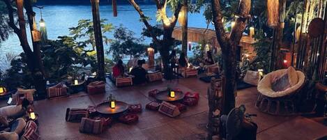 An outdoor seating area with tables and chairs, surrounded by trees and overlooking a body of water.