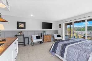 A bedroom with a large bed, a TV mounted on the wall, and a view of the outdoors through large windows. - The Chic Retreat - Studio for 2 (Branson)