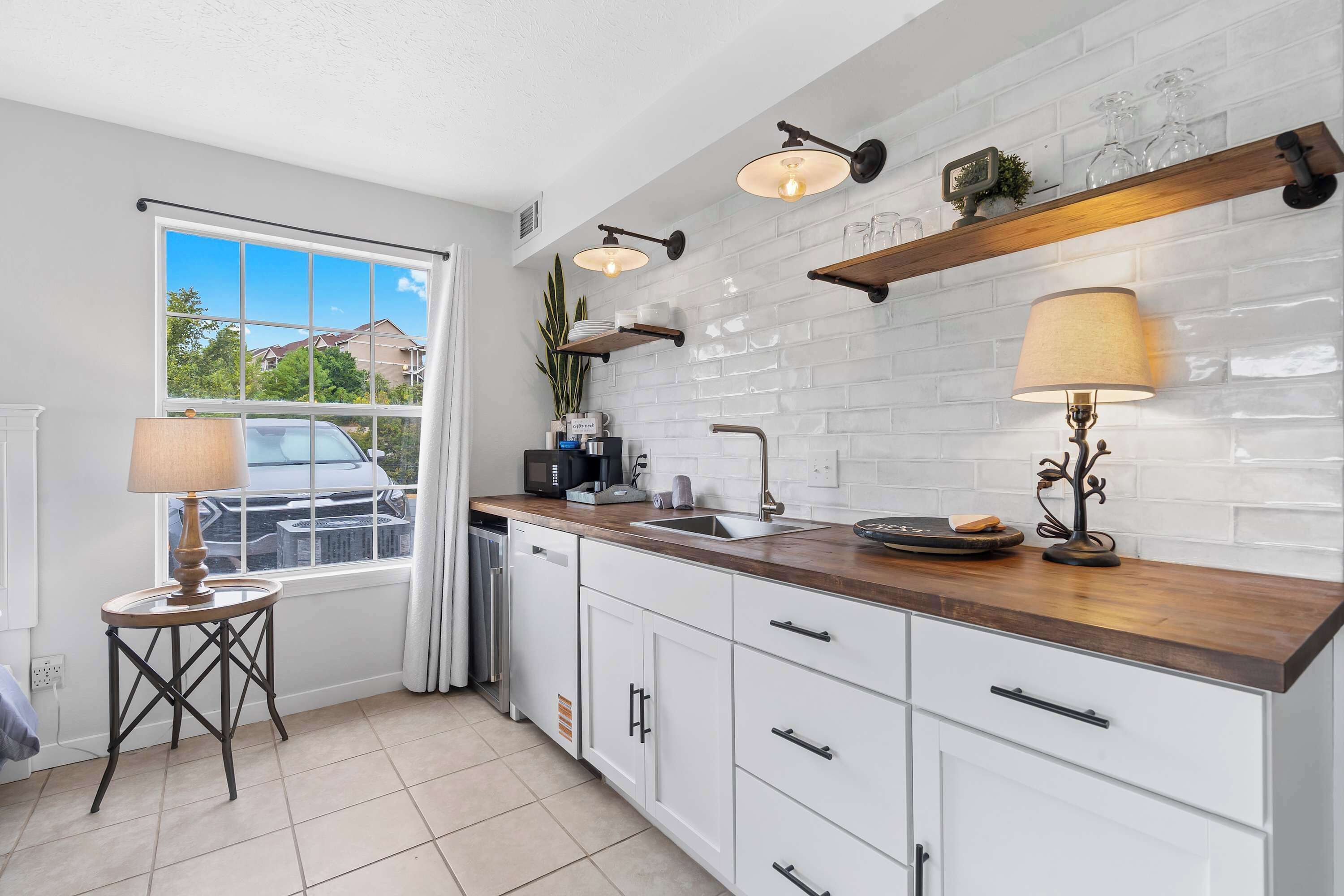 A modern kitchen with white cabinets, a wooden countertop, and a window with a view of houses.