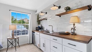 Une cuisine moderne avec des meubles blancs, un plan de travail en bois et une fenêtre donnant sur des maisons.