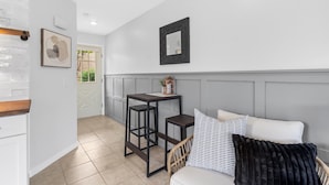 Une cuisine moderne avec des meubles blancs, un plan de travail en bois et un pare-feu en briques intégré. Une porte blanche donne accès à un espace patio.