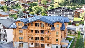 Un immeuble en bois à plusieurs étages, doté de balcons, d’un espace extérieur couvert et offrant une vue sur les maisons environnantes.