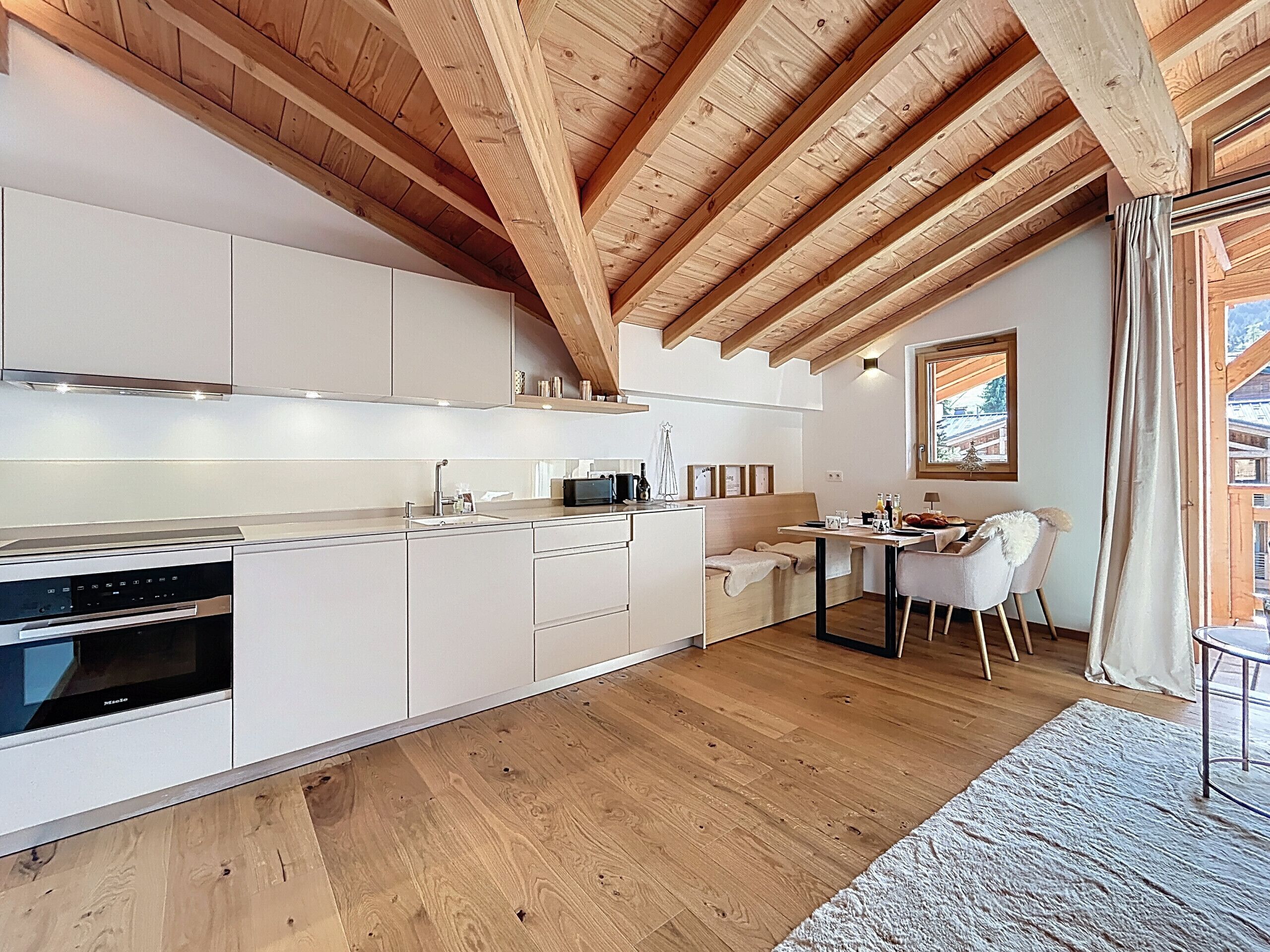 Une cuisine moderne avec des meubles blancs, des poutres en bois et un coin repas comprenant une table et des chaises.