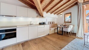 Une cuisine moderne avec des meubles blancs, des poutres en bois et un coin repas comprenant une table et des chaises.