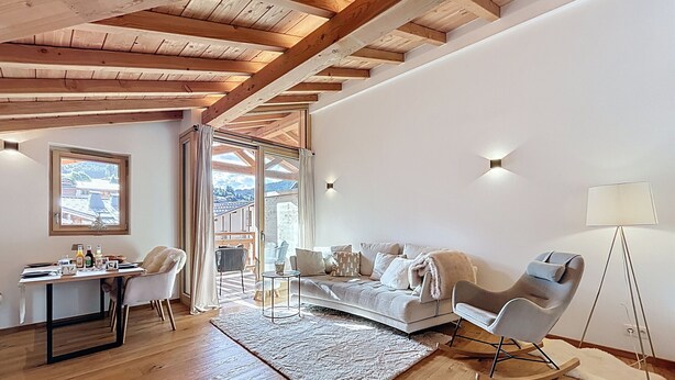 Un salon moderne avec des poutres en bois, un canapé, des fauteuils, une table à manger et une vue à travers une porte vitrée.