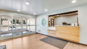 Un espace d’accueil avec un comptoir en bois, une porte d’entrée en verre et un logo sur le mur.
