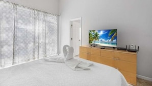Ein Hotelzimmer mit einem Bett, einem Fernseher auf einer Holzkommode und durchsichtigen Vorhängen.