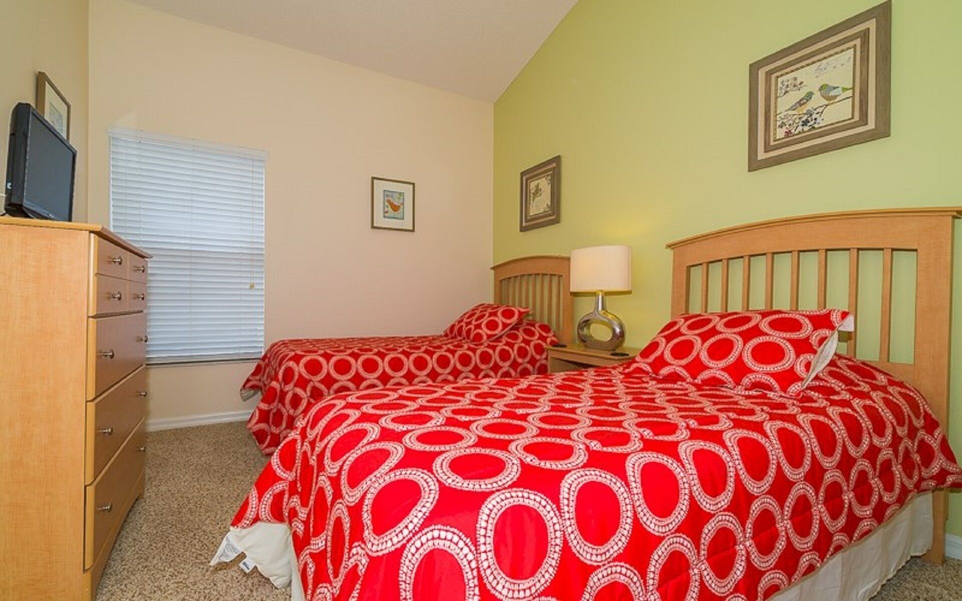 A bedroom with two beds, a dresser, a lamp, and framed pictures on the walls.