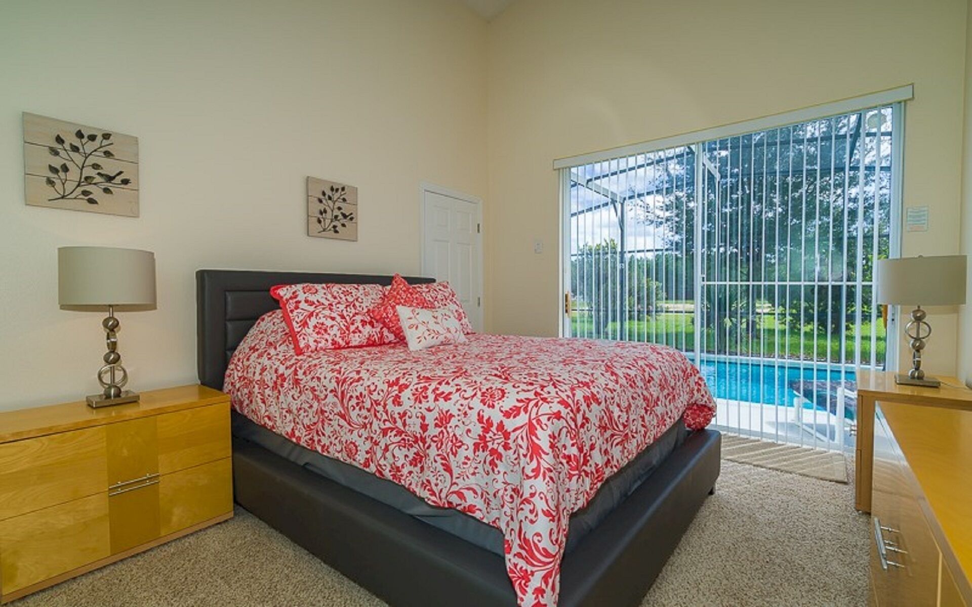 A bedroom with a bed, a nightstand, a dresser, and a window with a view of a swimming pool.