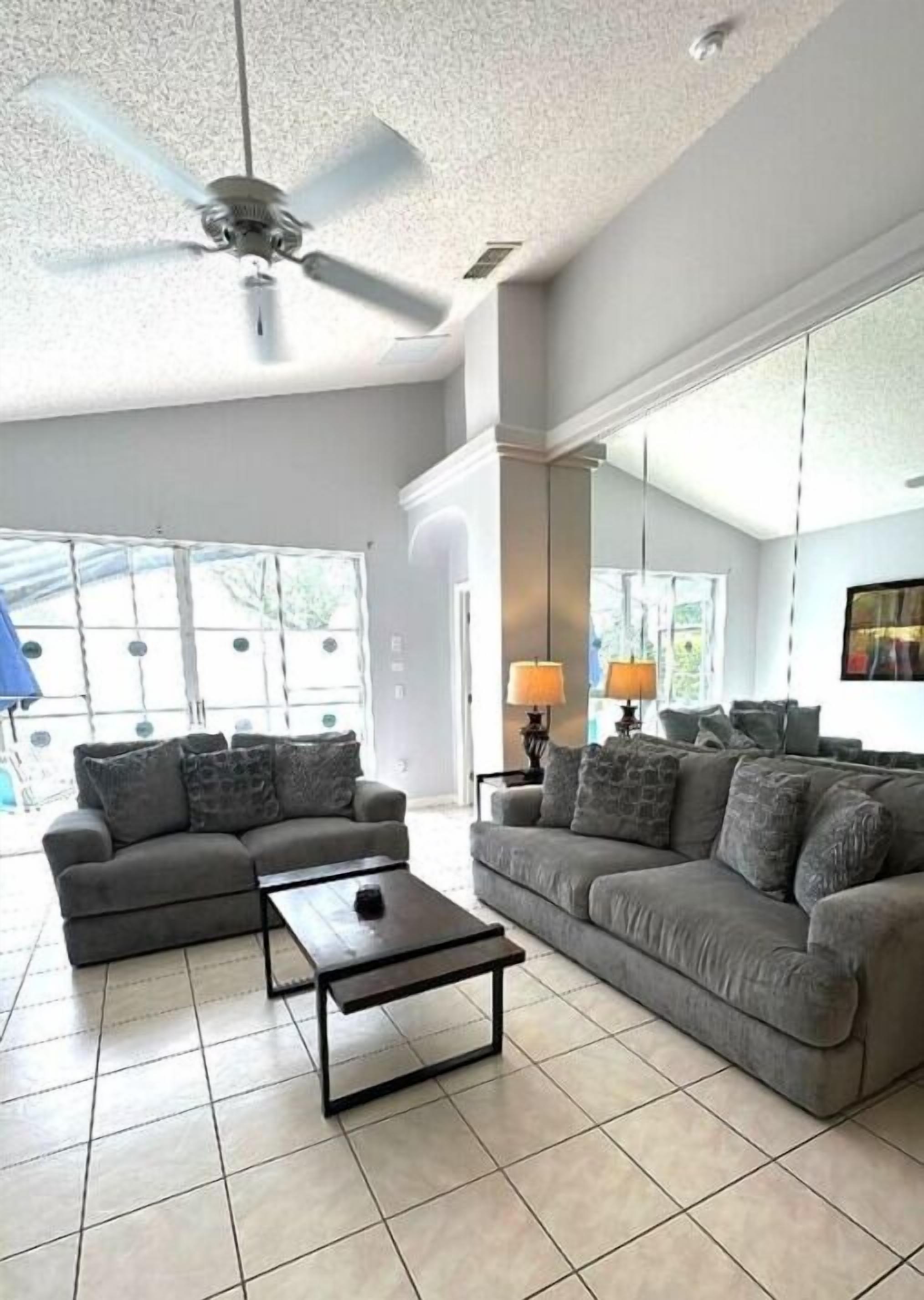A spacious living room with two grey sofas, a coffee table, and a ceiling fan.