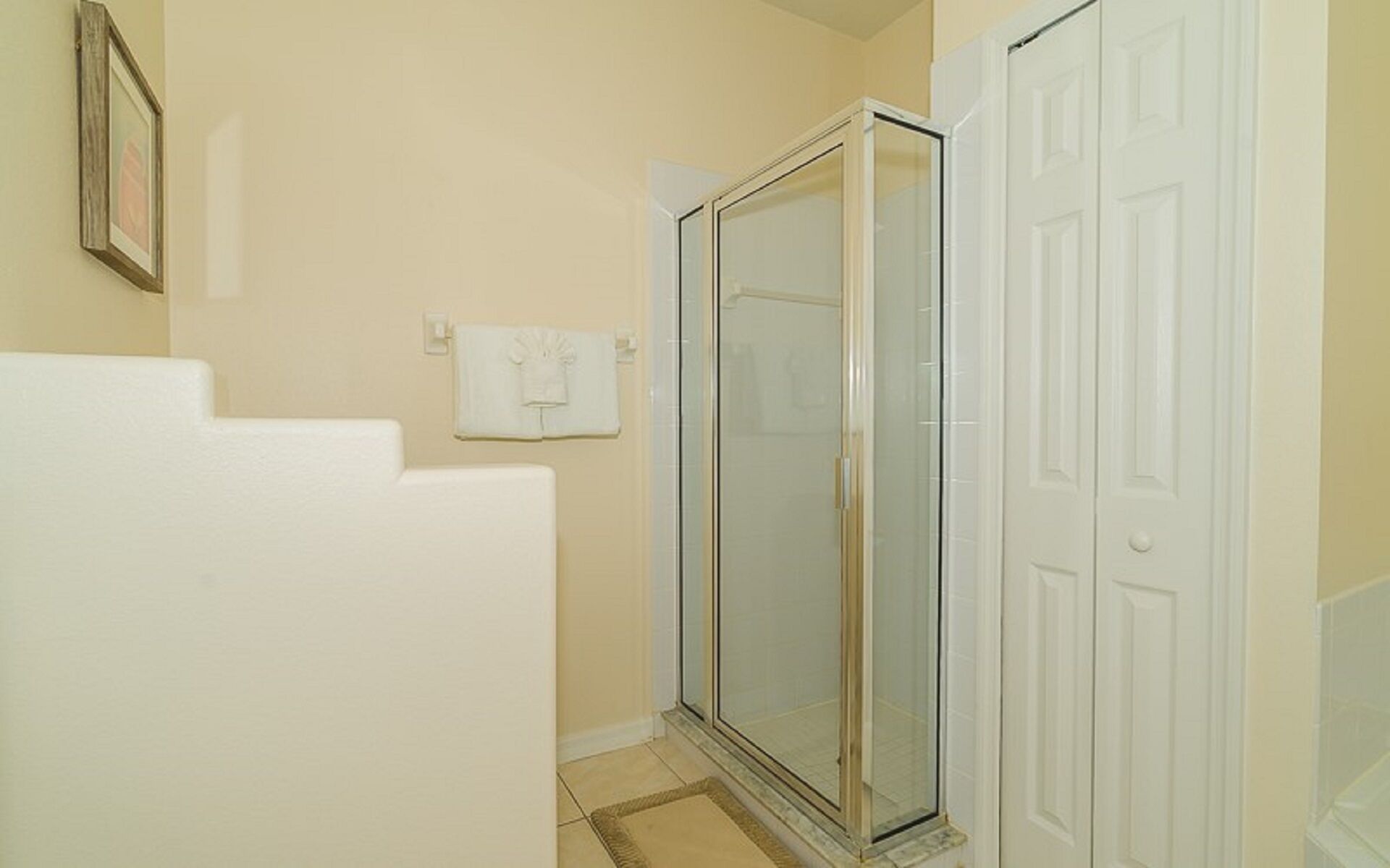 A bathroom with a glass shower enclosure, a white towel rack, and a white door.