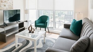 A modern living room with a sofa, a teal armchair, a coffee table, and a TV. - Premium one bedroom apartment fully furnished /Northyork (Toronto)