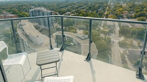 A balcony with a glass barrier, a white chair, and a table. - Premium one bedroom apartment fully furnished /Northyork (Toronto)