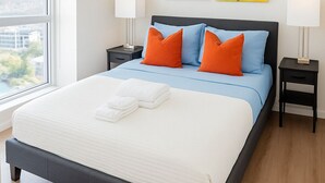 A modern hotel room with a large bed, two nightstands, a window with a city view, and two yellow paintings on the wall. - Premium one bedroom apartment fully furnished /Northyork (Toronto)