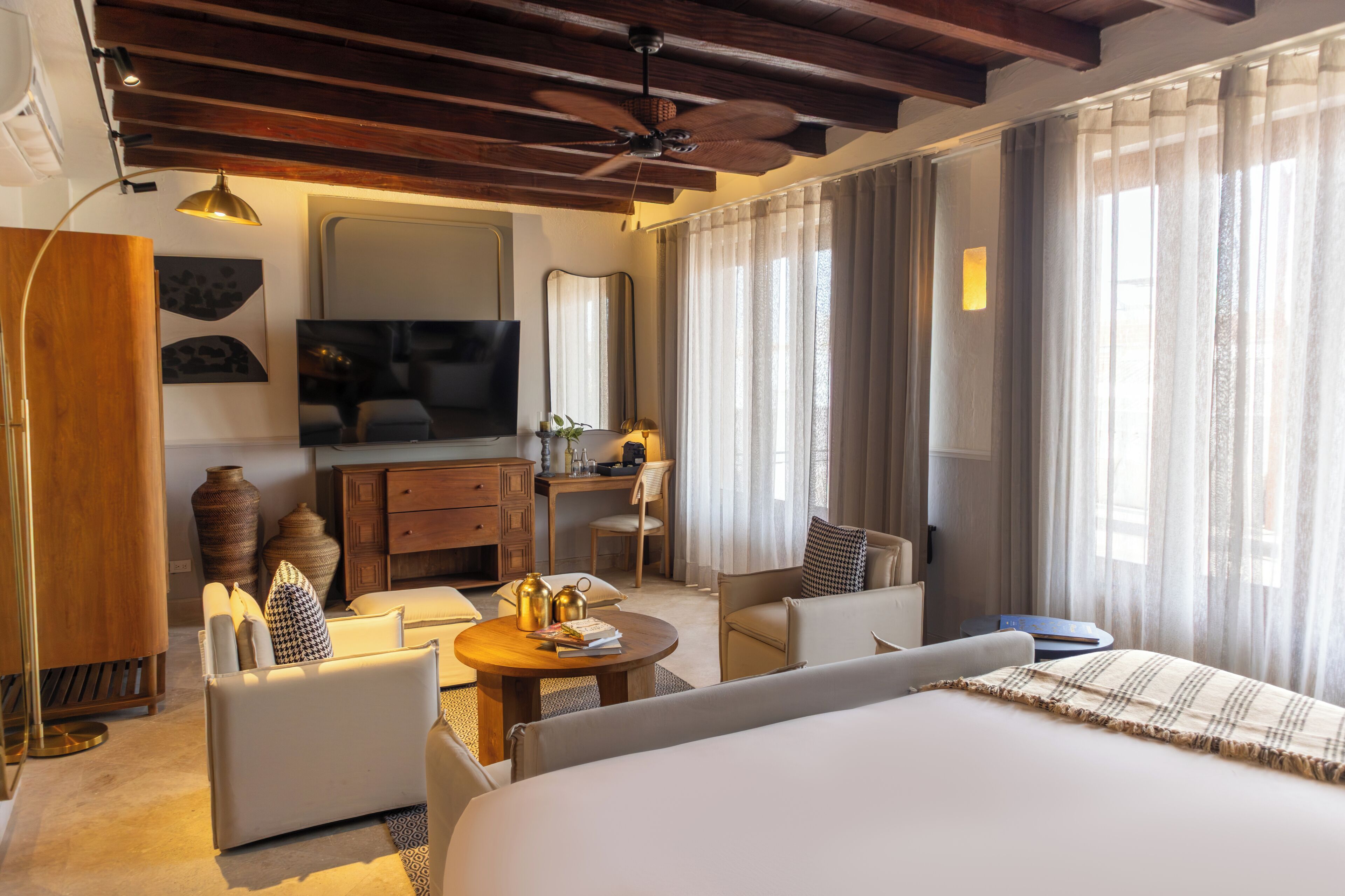 Una habitación de hotel con cama, escritorio, silla, sofá, televisor y ventilador de techo.