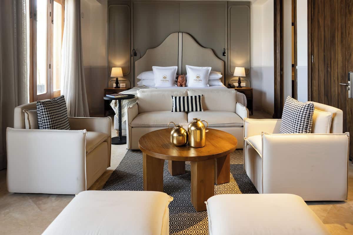 Una habitación de hotel con una cama, dos sofás, una mesita de centro y una mesita de noche con lámparas.