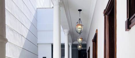Un pasillo con columnas blancas, suelo de mármol y barandilla de madera.
