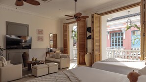 Habitación de hotel con una cama grande, un sofá, un televisor, un ventilador de techo y vistas al balcón exterior.