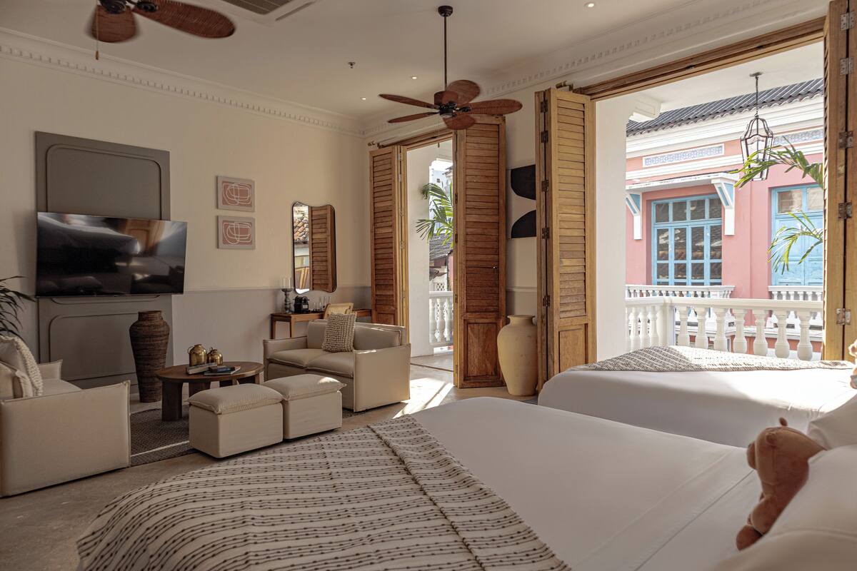 Habitación de hotel con una cama grande, un sofá, un televisor, un ventilador de techo y vistas al balcón exterior.