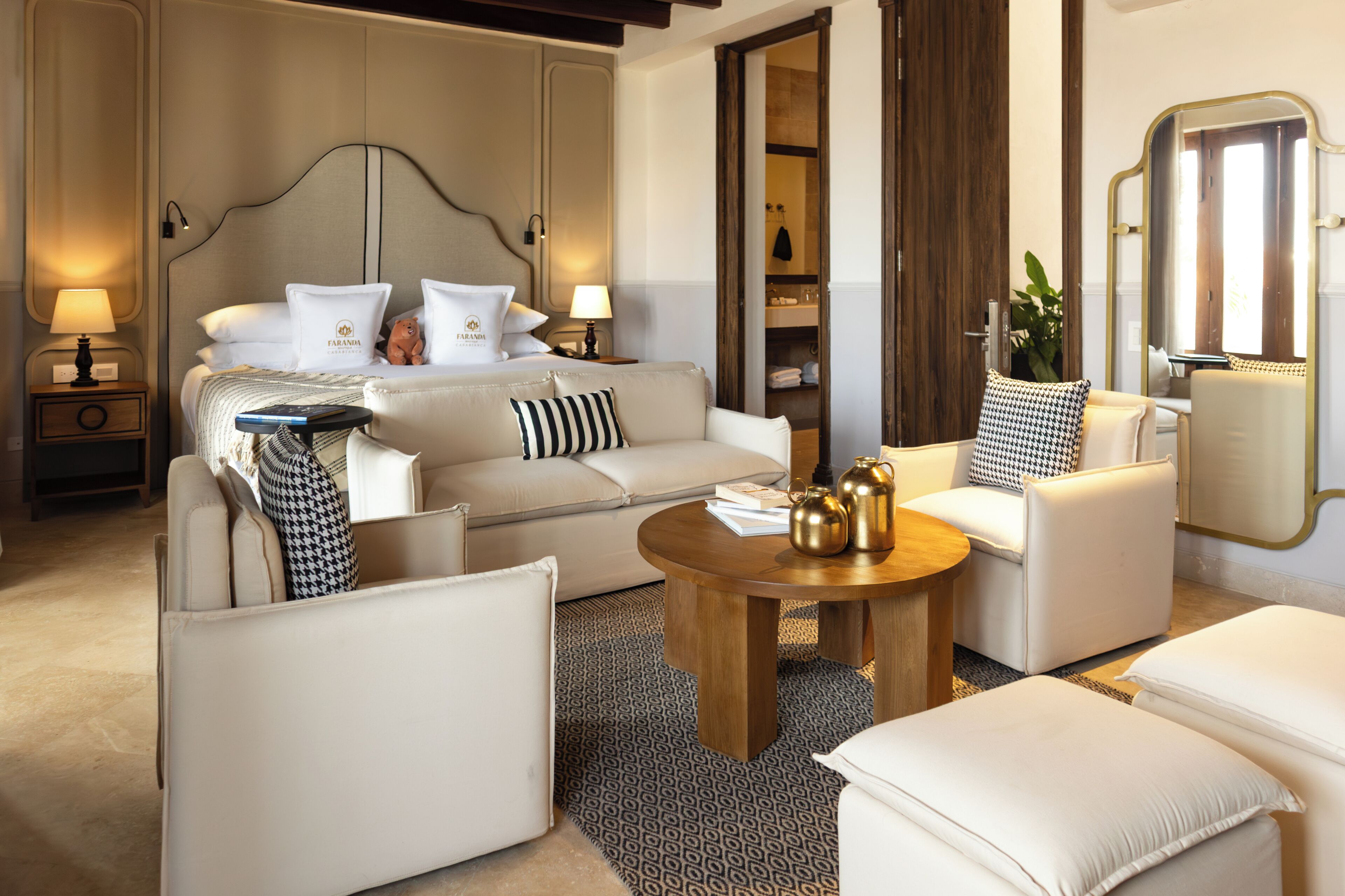 A hotel room with a bed, a sofa, a coffee table, a side table, and a mirror.