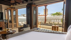Una habitación de hotel con una cama grande, un balcón con asientos y vistas a la ciudad.