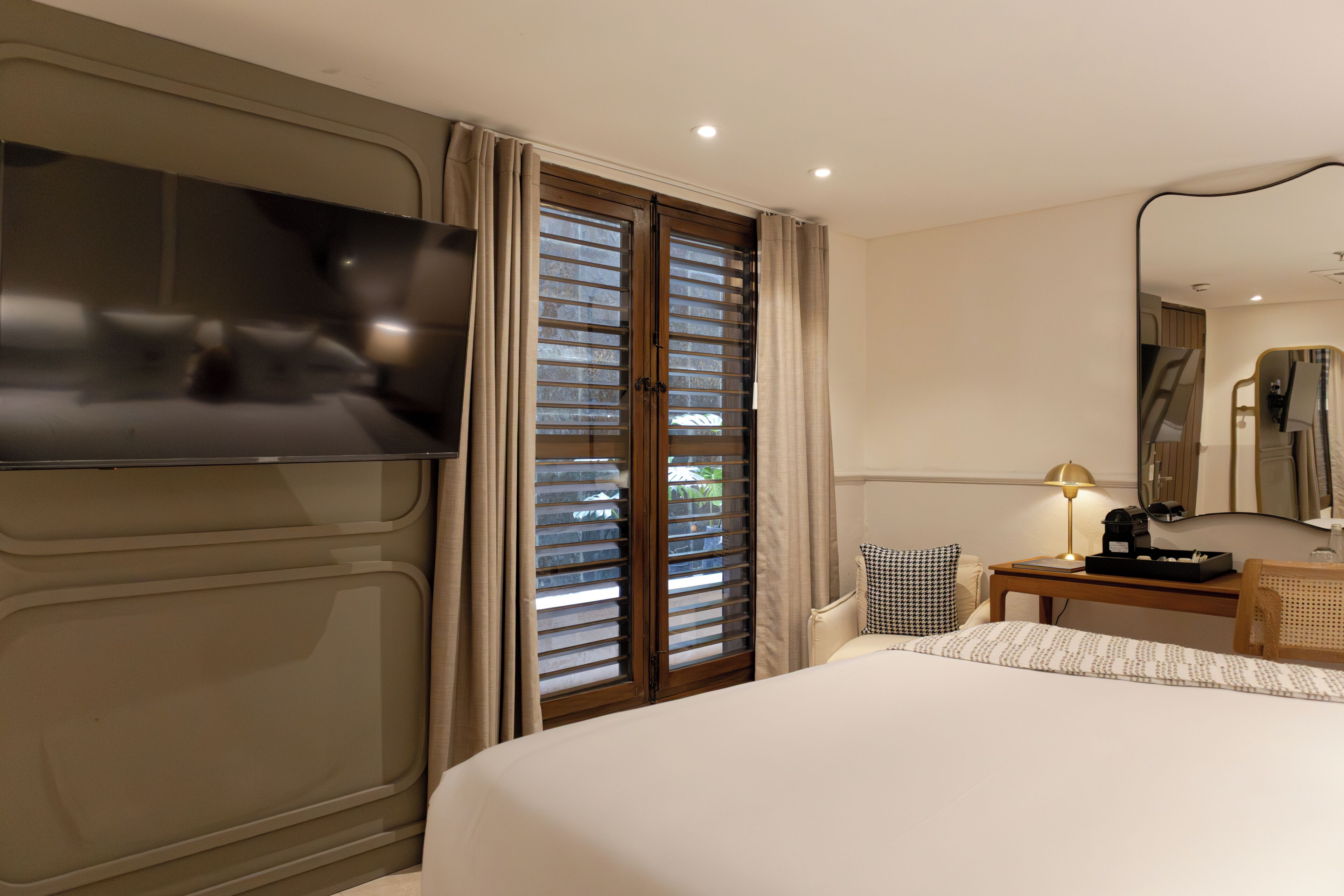 Habitación de hotel con cama, escritorio con lámpara, silla, televisión y ventana con persianas.