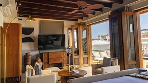 Una habitación amplia con ventilador de techo, un televisor de pantalla plana grande, un mueble de madera, un sofá y vistas a través de puertas de cristal grandes.