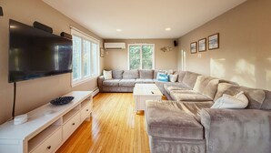 A modern living room with a flat-screen TV, a sectional sofa, a coffee table, and a white console table. - Chatham Family Retreat w/ Heated Pool (Chatham)