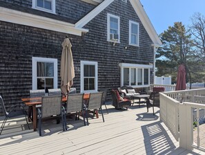A deck with outdoor furniture, including a table and chairs, and a covered area with an umbrella. - Chatham Family Retreat w/ Heated Pool (Chatham)