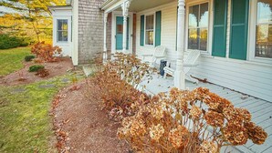 A two-story house with a porch, a stone chimney, and a garden with autumn foliage. - Chatham Family Retreat w/ Heated Pool (Chatham)