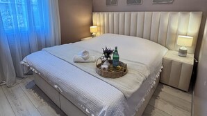 Un dormitorio moderno con una cama grande, dos mesitas de noche con lámparas, una ventana con cortinas y una obra de arte colgada en la pared.