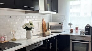 Una cocina moderna con armarios blancos y negros, horno empotrado, microondas y hervidor sobre la encimera.