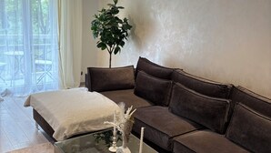 Una sala de estar moderna con una mesa de centro de vidrio, un sofá marrón, una manta color blanco y una planta en maceta.