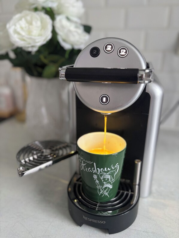 A Nespresso coffee machine with a green cup and a flower vase in the background.